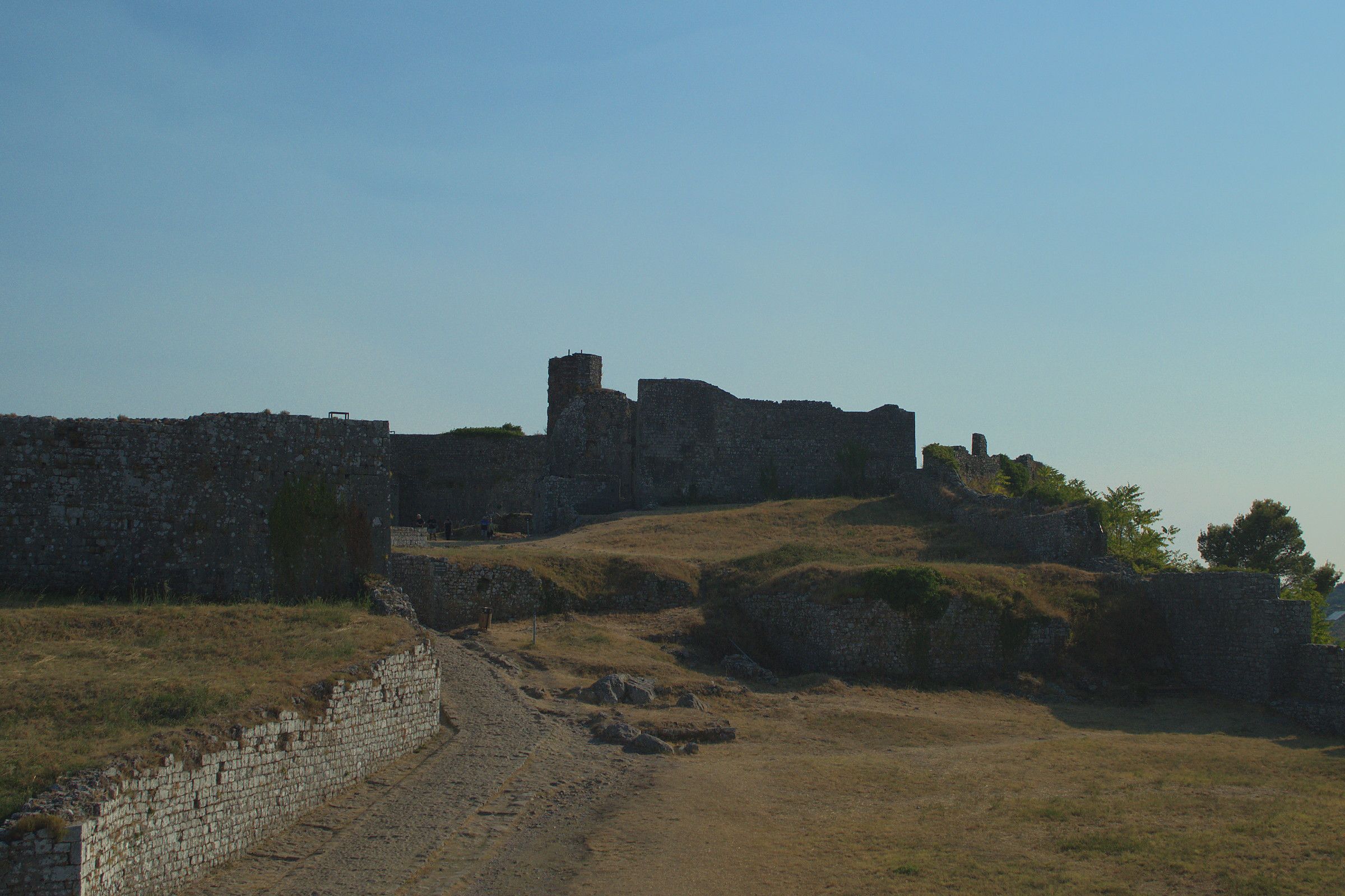 Le mura della fortezza di Rozafa a Scutari, con il sentiero sterrato che sale verso la sommità e la collina alle spalle