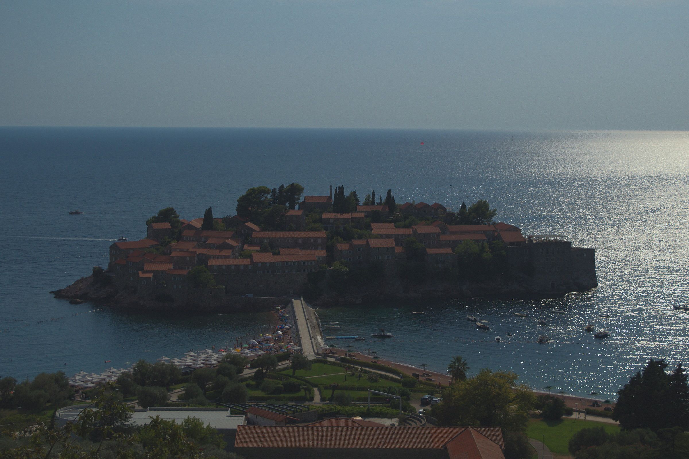 L'isolotto di Sveti Stefan visto dall'alto, con i tetti rossi stretti sulla roccia e l'istmo di sabbia che lo collega alla costa